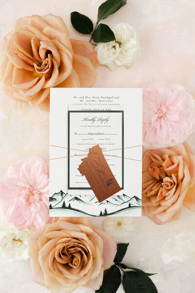 Assembled wedding invitation featuring a green mountain watercolor design and a copper Montana die-cut tag.