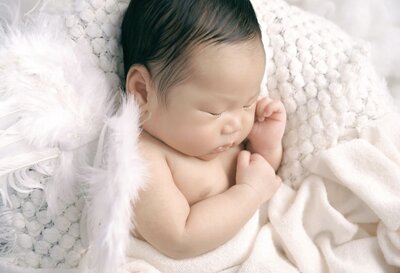 Newborn baby boy laying on a soft cream colored blanket and baby white baby wings on his back.