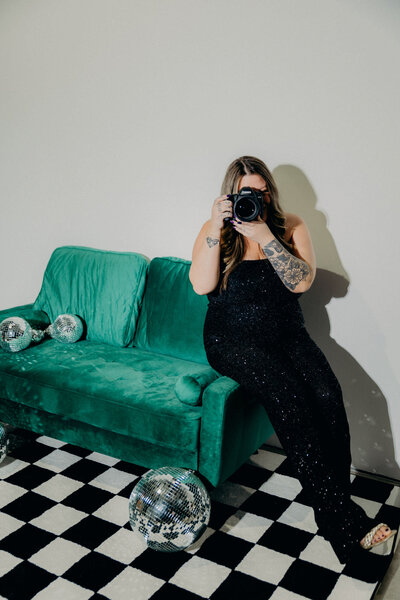 A woman, an Austin wedding photographer, sitting on a green velvet couch with a camera.