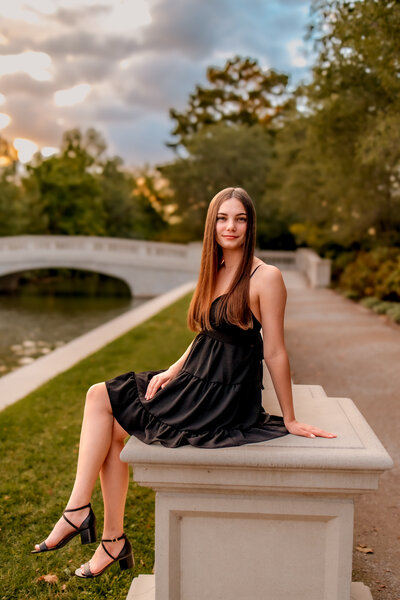 A gorgeous brunette girl is posing against a rock in Tower Grove Park for her senior portrait session.