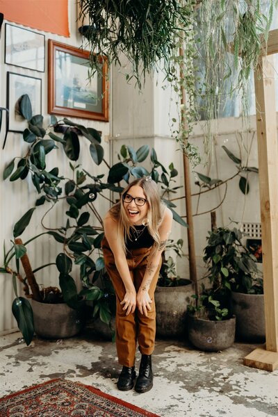 Smiling candid portrait of a down to earth wedding photographer in a leafy studio space.