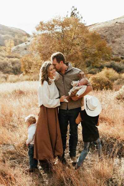 Family of three in a gorgeous warm Reno, NV field holding their newborn baby while their toddler sons run around.
