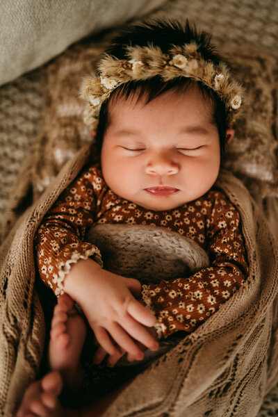 Newborn baby wrapped in rust-colored swaddle held by parents during lifestyle session at Moonlit Loft Studios in Riverside, California