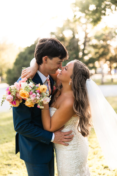 Bride and groom smiling and pulling each other close during golden hour wedding portraits at Hidden Vineyards in Maize, KS