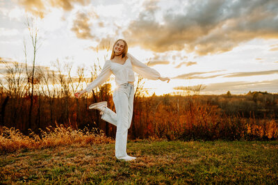 Girl wearing jeans and white shirt dancing in a field during sunset.
