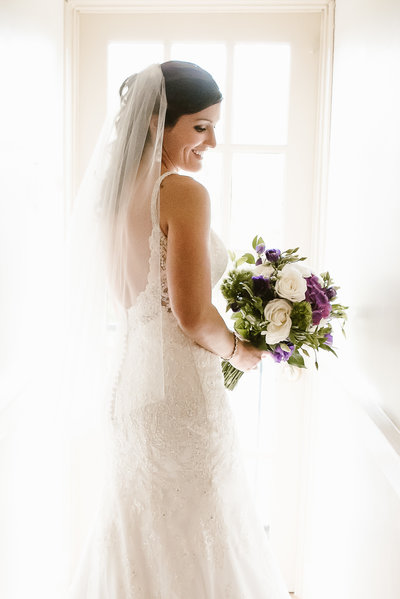 Bride looks over her shoulder in front of a window