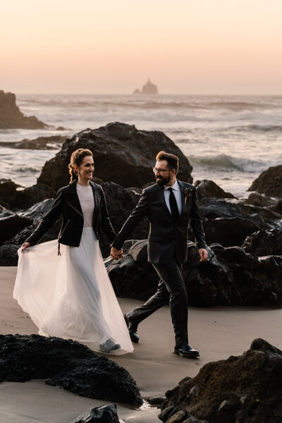 During their Oregon coast elopement, a couple in their wedding attire explores a rocky beach.