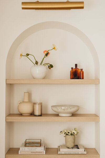 Close-up of arched built-in shelf with minimalist decor, neutral ceramics, and floral accents in a modern Montreal interior – by Ingrid Interior Design.