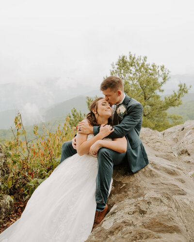 bride and groom cuddled on the rocks in Shenandoah National Park in the summer rain