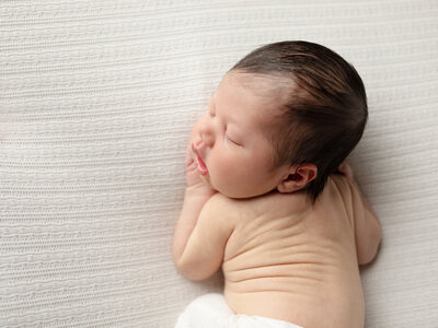 newborn baby boy posed on white fabric for newborn photoshoot