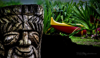 A large wooden tiki god in front of an outrigger canoe in a tropical Hanalei, Kaua’i garden.