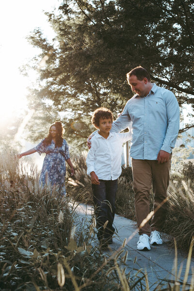 family of 3 walking through tall grass on the waterfront of queens new york during golden hour 