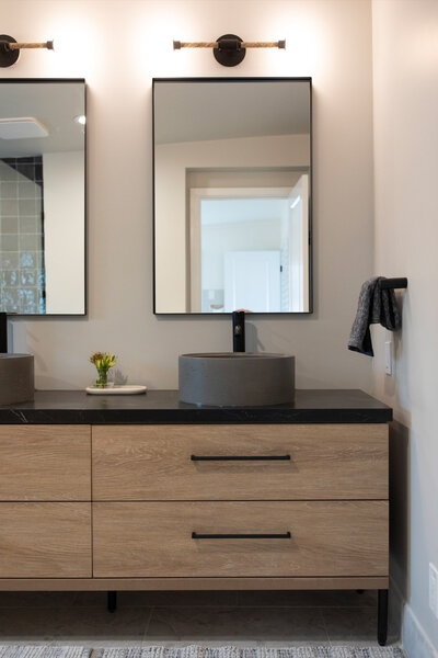 Beach house interior design details of the primary bathroom featuring a vanity with double sinks, modern sink basins and mirrors.