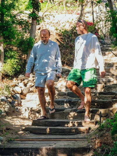 Two older men walking down stone steps under dappled lighting