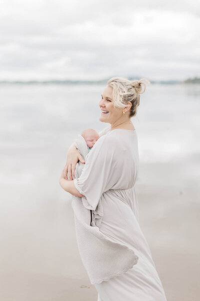 A new mum on the beach cradling her new baby during family portraits.