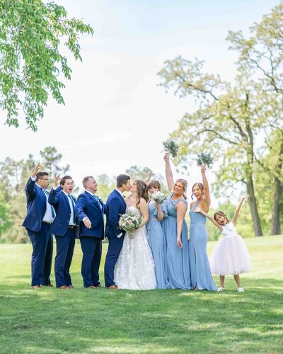 bride and groom on golf course with bridesmaids and groomsman standing next to them wearing blue dresses and blue tuxedos 