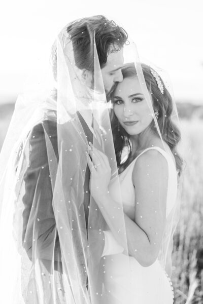 bride and groom posing while wrapped in wedding veil