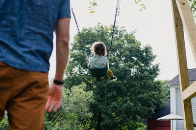 Documentary family photography with child swinging outdoors and parent nearby