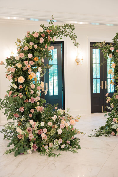 Indoor floral arch with pink and white roses, green foliage.