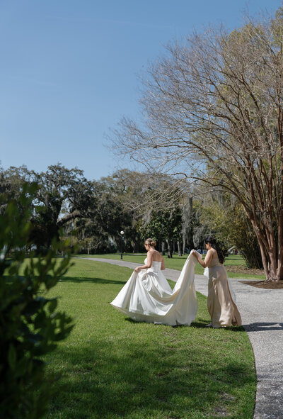 Bridesmaid holding dress and walking with Bride on wedding day taken by east coast wedding photographer Shelby Ann Photos