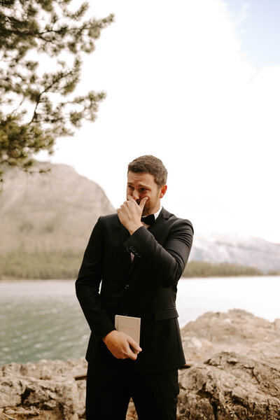Groom crying tears of joy as he sees his bride for the first time with Moraine lake and the mountains of Banff National Park Canada behind him