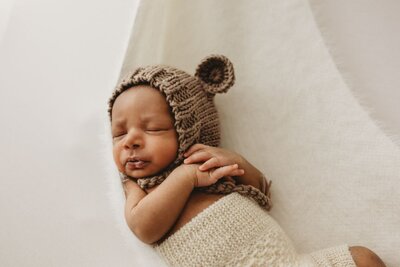 A newborn baby smiles while sleeping, wearing a white floral headband and a crochet wrap