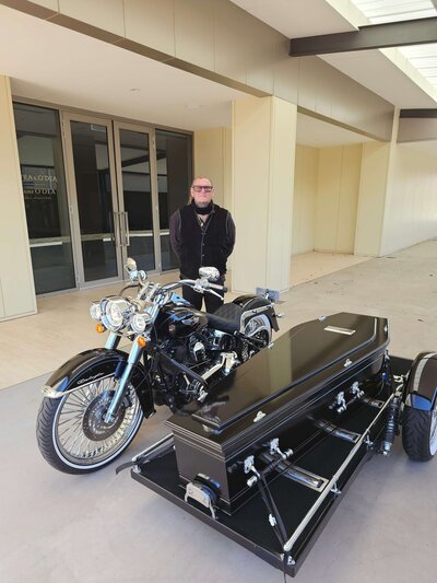 Ben standing behind the Harley Davidson hearse, reflecting the passion and dedication behind Caskets and Chrome.