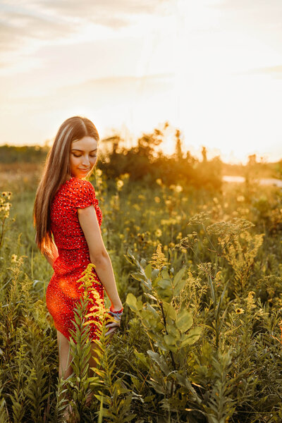 girl in red dress looking down at shoulder in a field at sunset