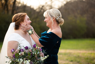 Mother of bride lovingly holding her daughters face on her wedding day