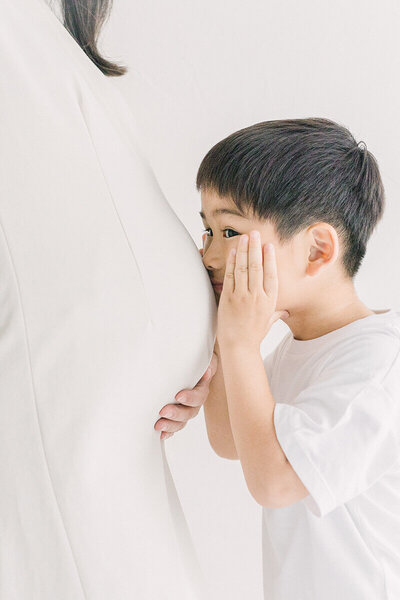 ママの大きなおなかに話しかけるようにしてキスしている男の子の可愛いマタニティフォト