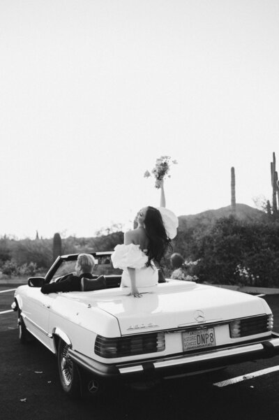 Bride celebrating elopement by throwing florals in the air from the back of a vintage car