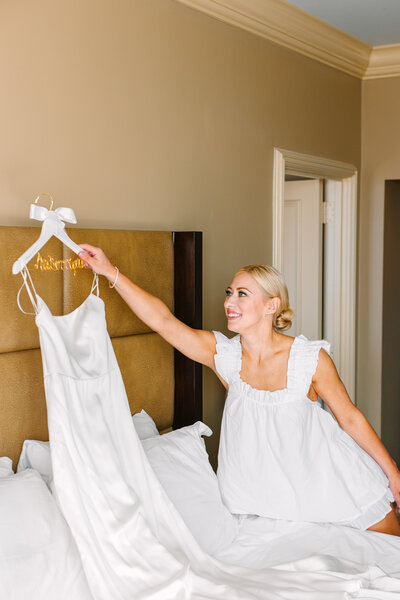 Bride in her pajamas hanging up her wedding gown above a bed