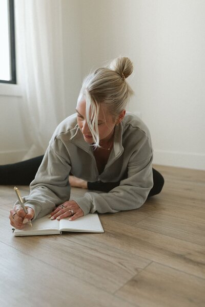 Woman journaling on the floor in soft natural light, practicing a daily ritual of mindful reflection