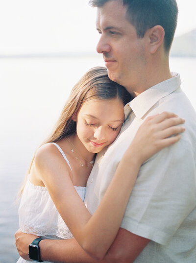 Tween daughter rests head on father's chest at the morning sun casts an ethereal glow on her face, documented on film