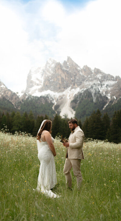 Groom saying his vows during their Dolomites Elopement in an alpine meadow with huge snow covered mountains behind them