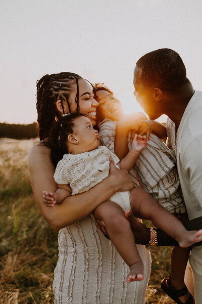 A family of four laughs and hugs on a hill at sunset in plano, texas