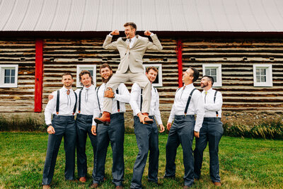 Groomsmen holding groom up near red barn at Staubach Creek Ranch in Winston, MT