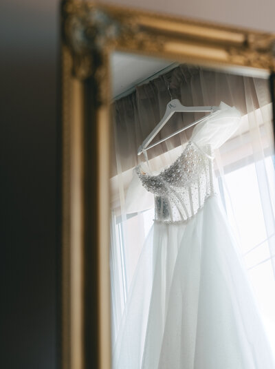 Wedding dresses displayed on hangers in a bridal boutique with soft natural light filtering through sheer curtains.