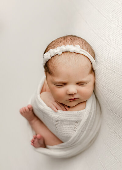 baby girl posed on all white fabric in our denver newborn photography studio