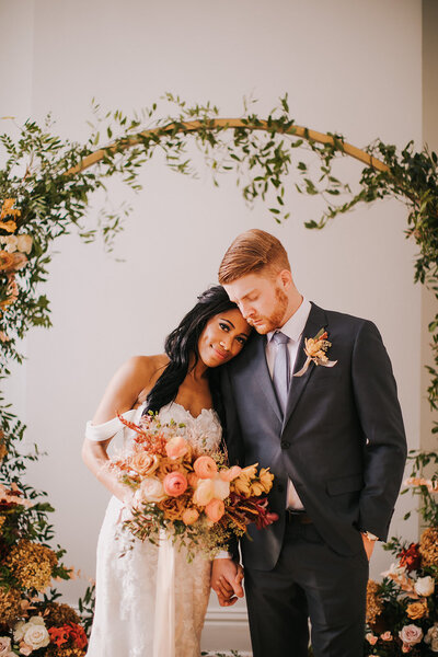 A bride and groom stand under a circular floral arch at The Covenant at Murray Mansion