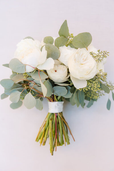 Beautiful bridal bouquet featuring lush white peonies and delicate eucalyptus leaves, combining soft greenery with an elegant touch for a timeless wedding accessory.