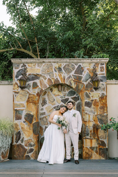 Bride and groom pose together in front of the rocked wall on the Lakeside at Wolf Lakes Park