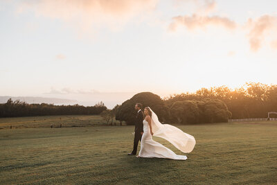 bride and groom holding hands in field with sunset in background