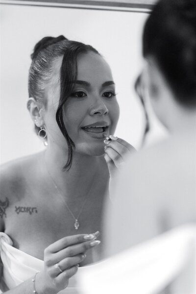 A person looking in a mirror and putting on lipstick 