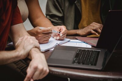 three people sitting around a meeting table in front of a laptop