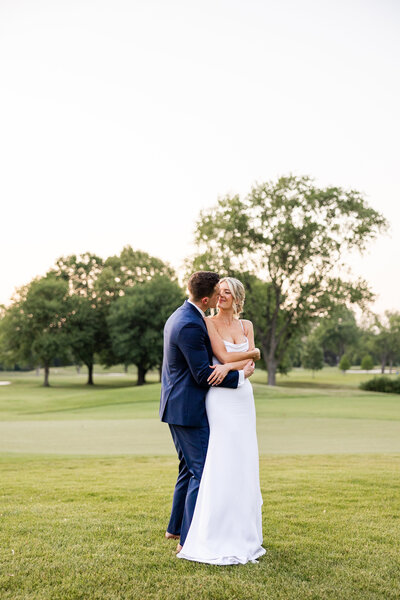 Bride and groom embracing on a green lawn