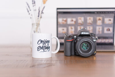 A desk with a D750 DSLR, laptop, and a mug that says "Coffee & Editing".