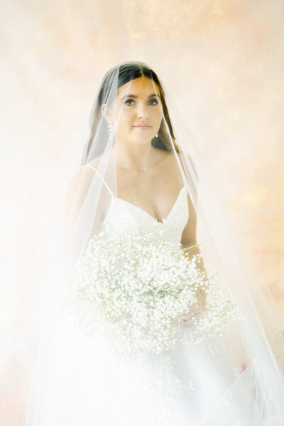bridal portrait with veil and wedding bouquet in studio against pink backdrop