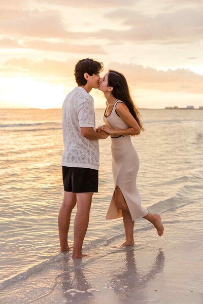 Man and woman kiss in the shoreline with a golden sunset