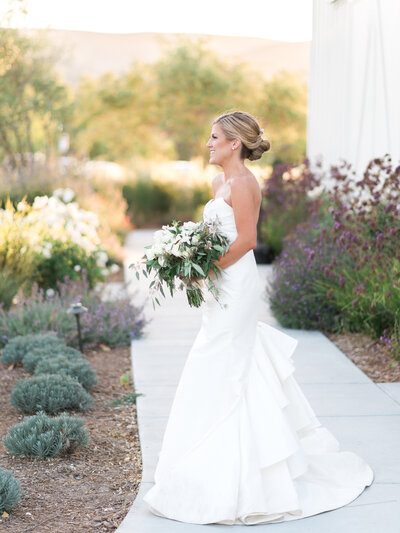 Bride in white wedding dress walking through garden with bouquet